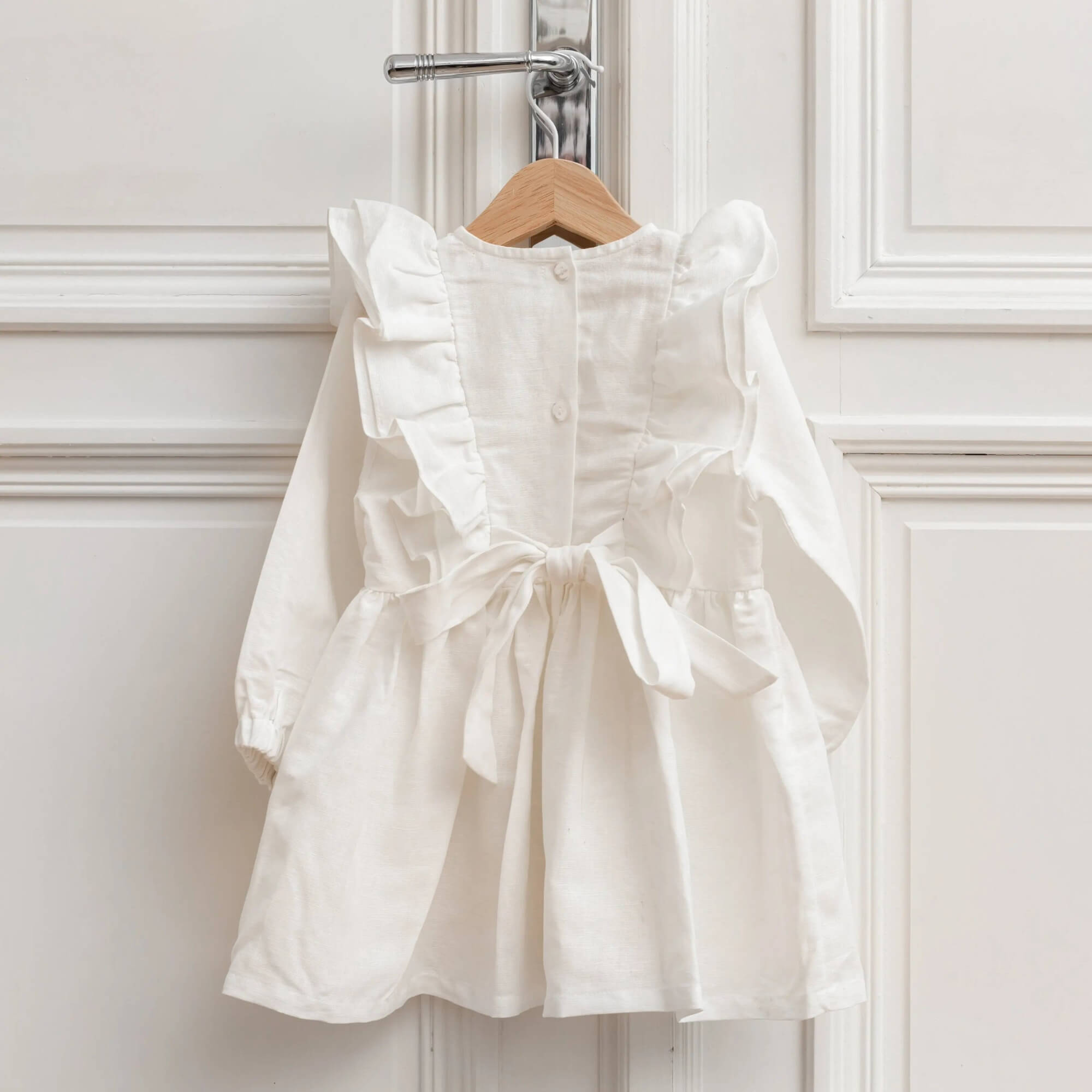 White linen baby dress hanging with button back and tie bow detail