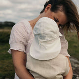 Baby wearing white linen sun hat with neck protection outdoors, lifestyle parent-child moment