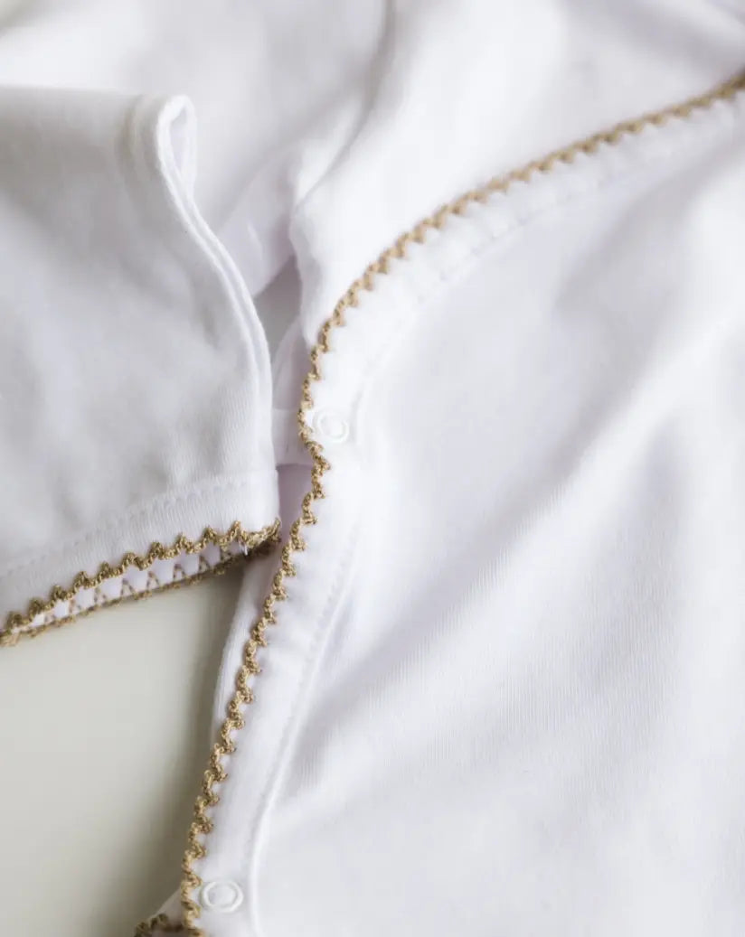 Close-up of caramel brown crochet trim on the white baby bodysuit.