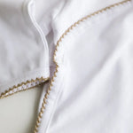 Close-up of caramel brown crochet trim on the white baby bodysuit.