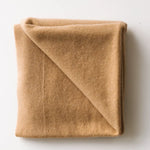 Caramel brown baby cashmere blanket neatly folded on a white surface.