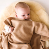 Baby cuddled in a caramel brown cashmere blanket, lying on a soft cream pad.