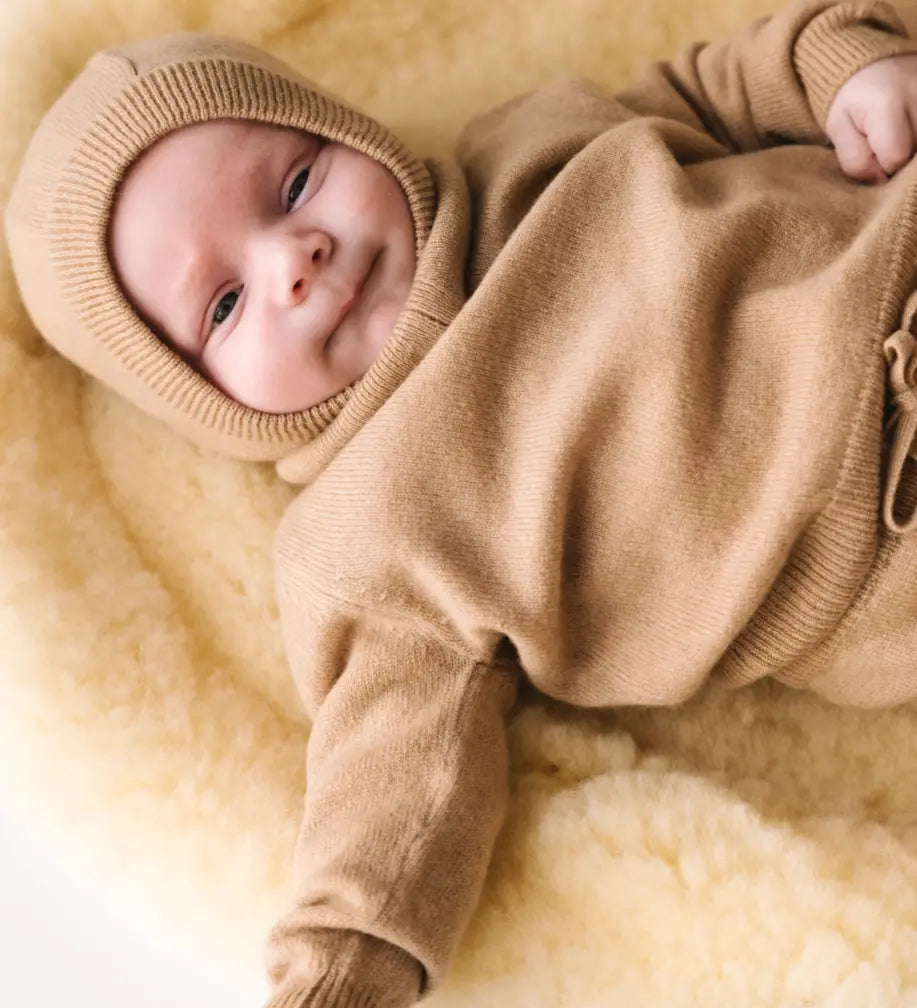 Baby lying on a soft cream blanket wearing a caramel brown cashmere sweater.