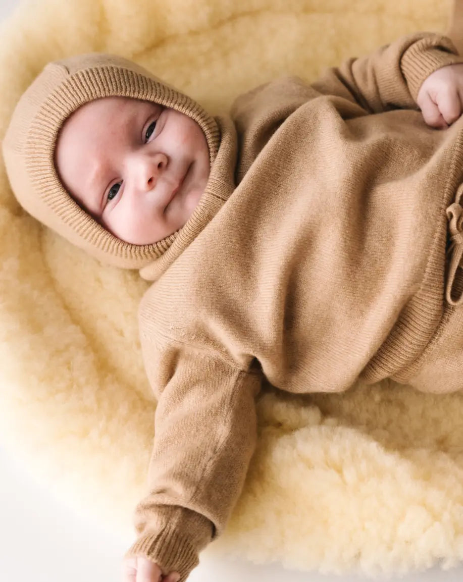 Baby lying on a soft cream blanket wearing a caramel brown cashmere sweater.