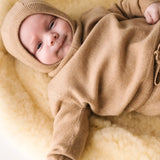 Baby lying on a soft cream blanket wearing a caramel brown cashmere sweater.