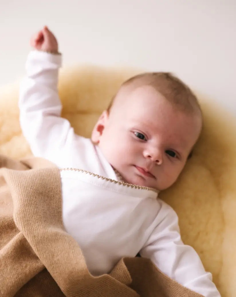 Baby lying on a blanket wearing a white bodysuit with caramel brown crochet trim.