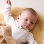 Baby lying on a blanket wearing a white bodysuit with caramel brown crochet trim.