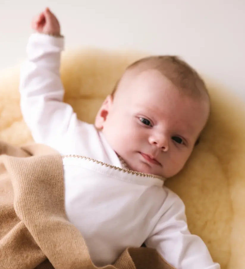 Baby lying on a blanket wearing a white bodysuit with caramel brown crochet trim.