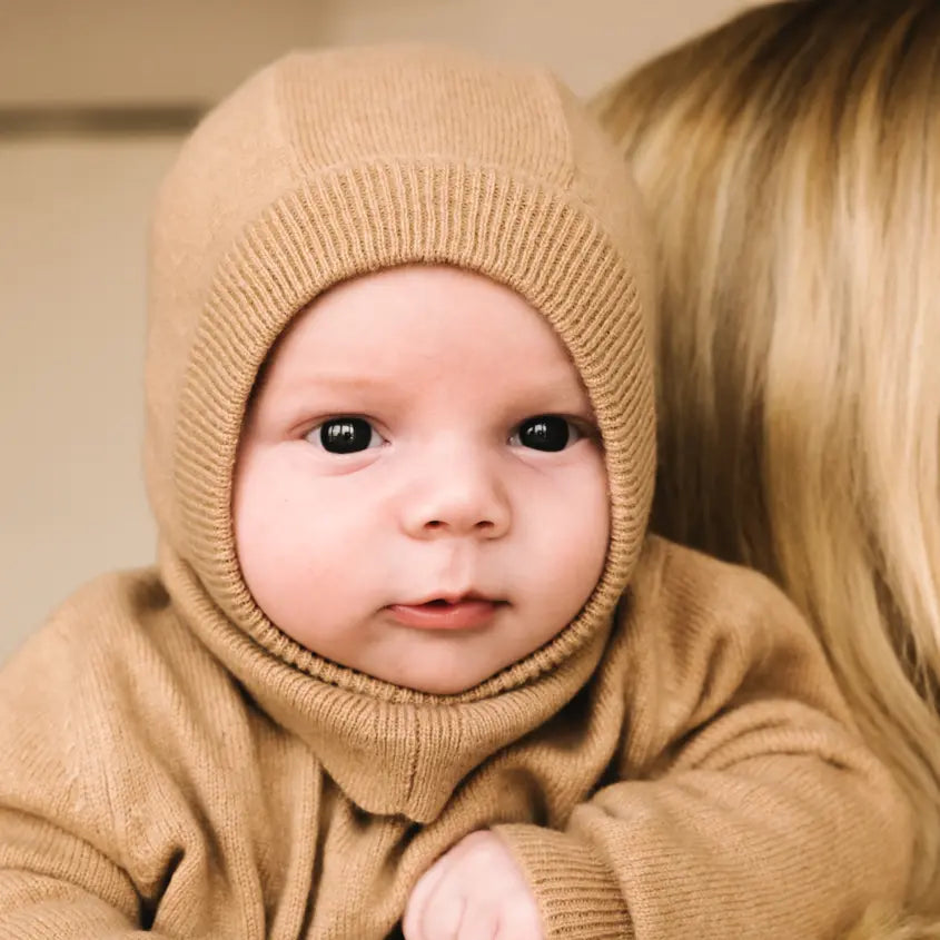 Baby wearing soft caramel brown cashmere balaclava, warm knitted hood for infants.