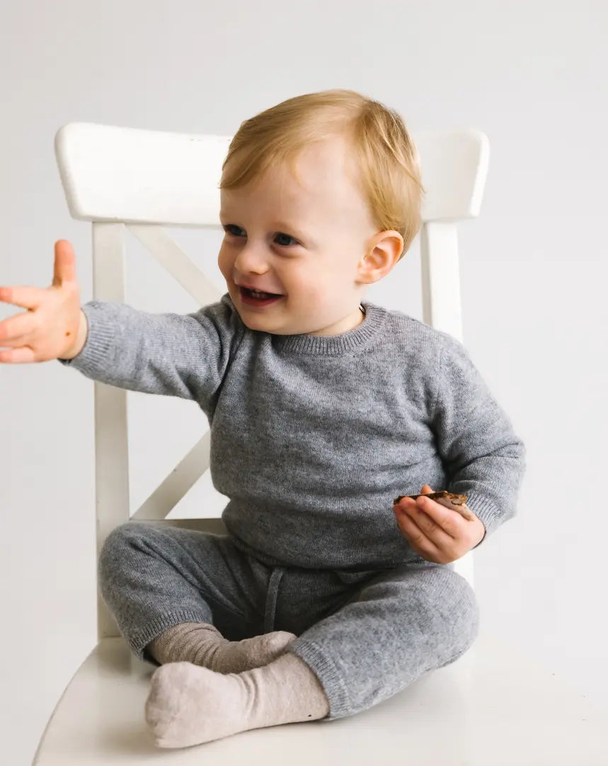 Toddler wearing a heather grey baby cashmere sweater sitting on a chair